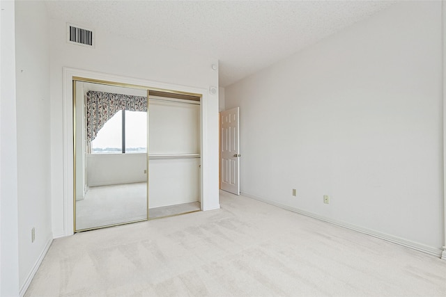 unfurnished bedroom with baseboards, visible vents, a textured ceiling, carpet flooring, and a closet