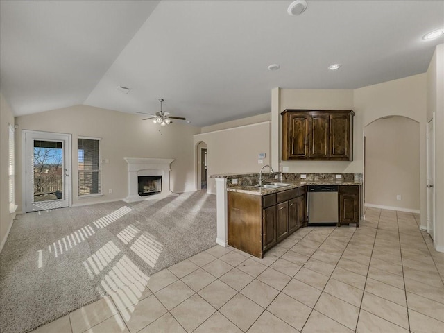 kitchen with arched walkways, light colored carpet, a fireplace with raised hearth, stainless steel dishwasher, and dark brown cabinetry