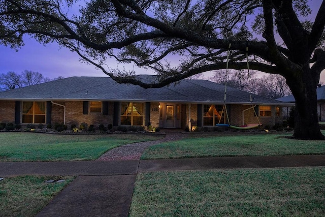 ranch-style home featuring a shingled roof, brick siding, and a front lawn