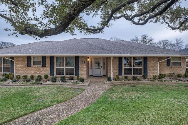 single story home with a shingled roof, a front lawn, and brick siding