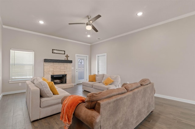 living room featuring ornamental molding, a stone fireplace, baseboards, and wood finished floors