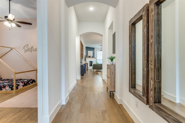 hallway with baseboards, arched walkways, and wood finished floors