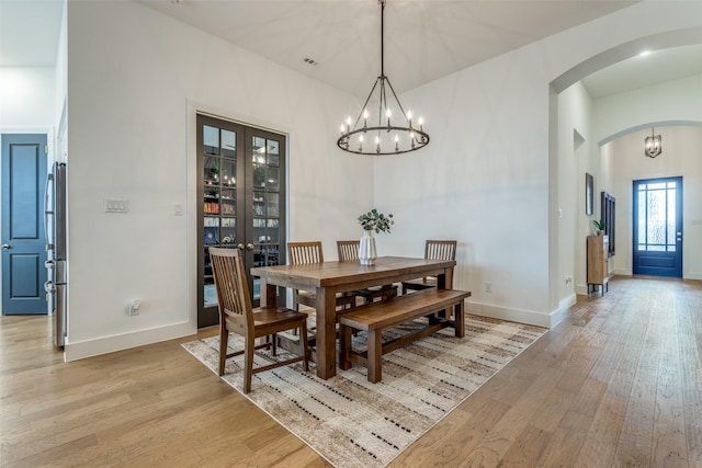 dining space with light wood-style floors, baseboards, arched walkways, and a notable chandelier