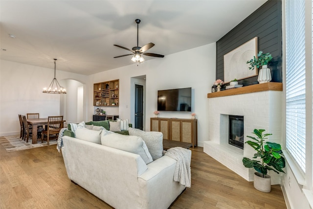 living area featuring ceiling fan with notable chandelier, arched walkways, a fireplace, and wood finished floors