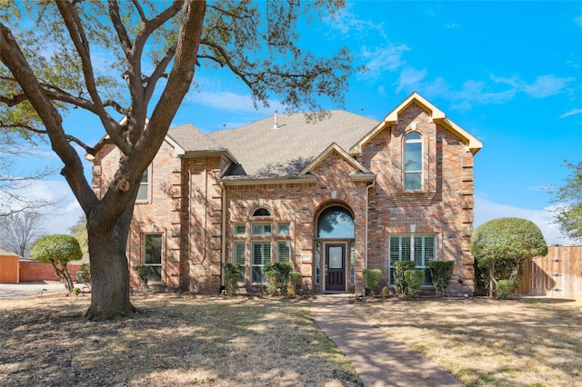 traditional-style home with roof with shingles, fence, and brick siding