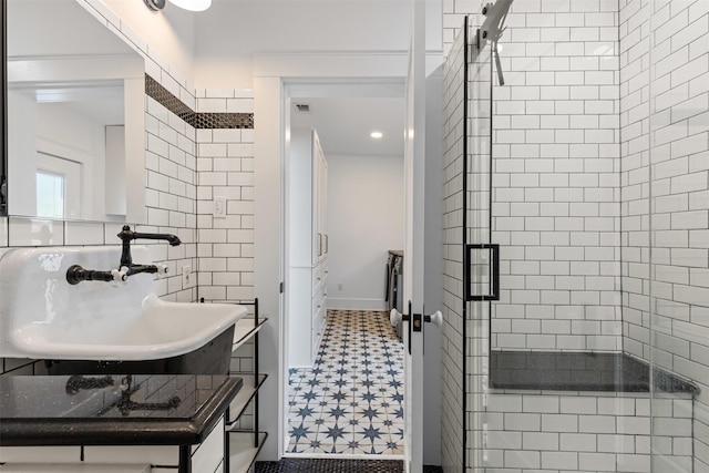 bathroom featuring a stall shower, visible vents, tile patterned floors, a sink, and tile walls