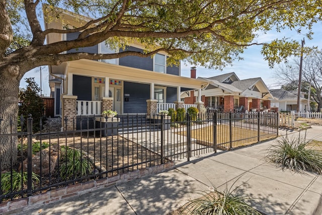 view of front of home featuring a fenced front yard, a residential view, covered porch, and brick siding