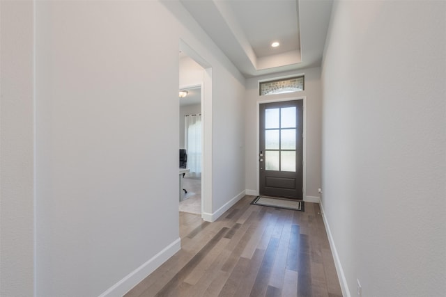 doorway with a tray ceiling, baseboards, wood finished floors, and recessed lighting