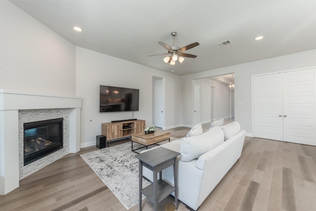 living room featuring visible vents, a stone fireplace, baseboards, and wood finished floors