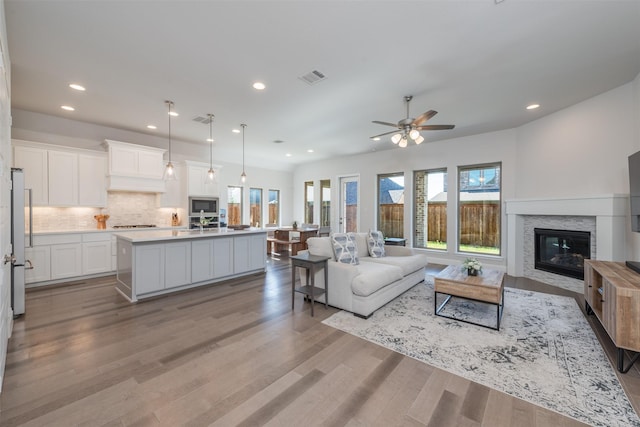 living area with light wood-style floors, a glass covered fireplace, visible vents, and recessed lighting