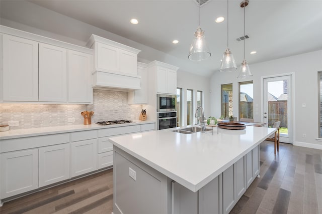 kitchen featuring stainless steel appliances, a sink, visible vents, decorative backsplash, and an island with sink