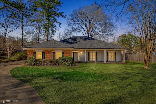 ranch-style home featuring brick siding, fence, french doors, roof with shingles, and a front lawn