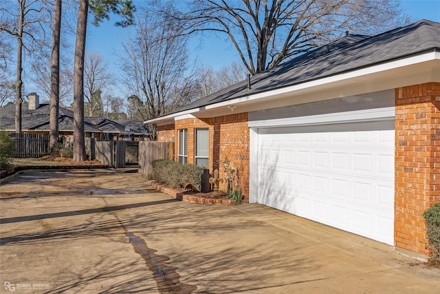 view of side of home featuring brick siding, driveway, an attached garage, and fence