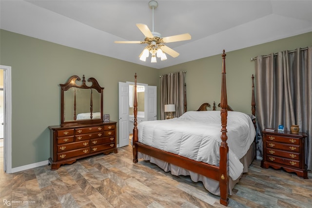 bedroom with a ceiling fan, stone finish floor, baseboards, and ensuite bathroom