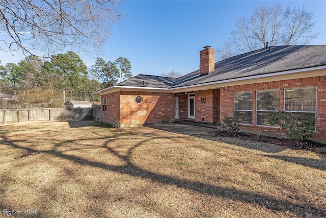 back of property featuring a chimney, fence, a lawn, and brick siding