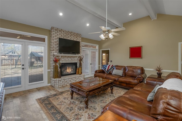 living area featuring a ceiling fan, lofted ceiling with beams, wood finished floors, french doors, and a brick fireplace