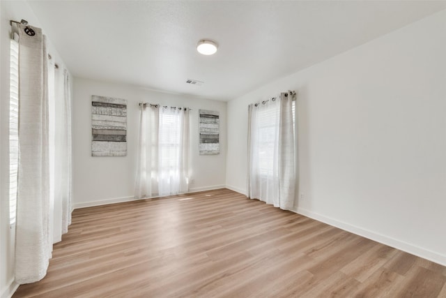 empty room featuring light wood-style floors, baseboards, and visible vents