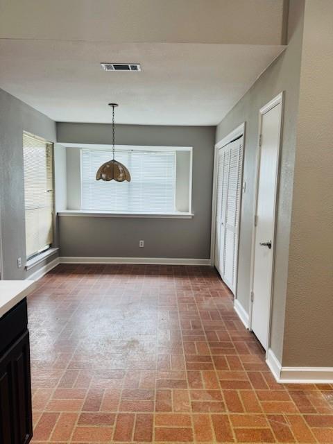 unfurnished dining area with brick floor, visible vents, and baseboards