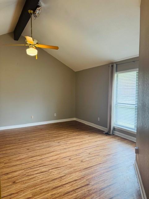 empty room with vaulted ceiling with beams, ceiling fan, baseboards, and wood finished floors