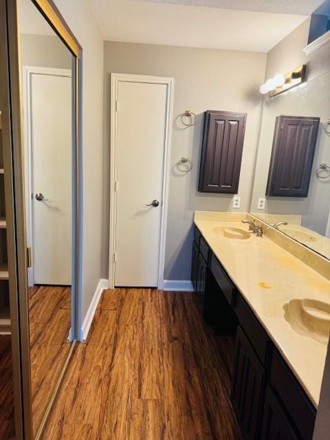 bathroom with a sink, double vanity, baseboards, and wood finished floors