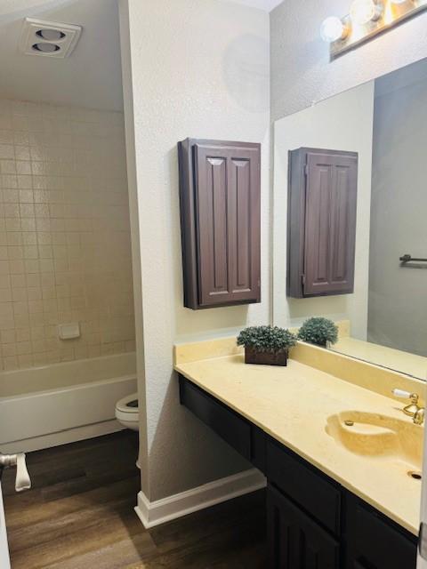 full bath with baseboards, toilet, wood finished floors, vanity, and shower / washtub combination