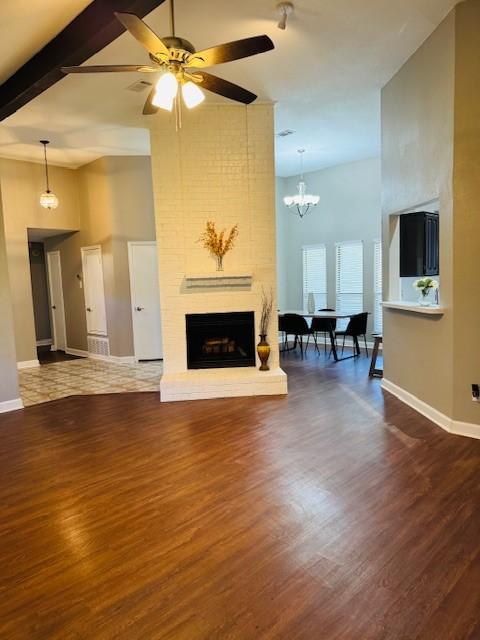 living area featuring baseboards, a brick fireplace, wood finished floors, and a towering ceiling