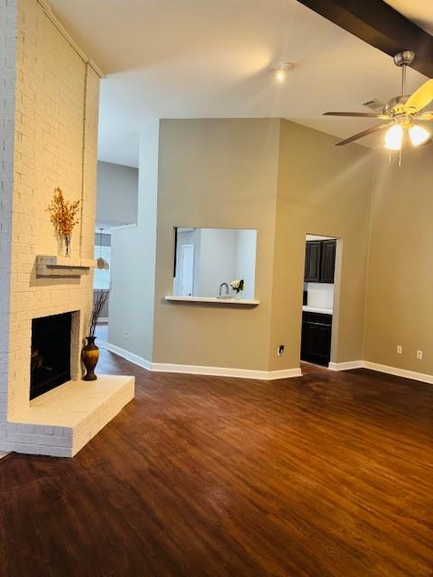 unfurnished living room featuring ceiling fan, dark wood-type flooring, a fireplace, baseboards, and beamed ceiling