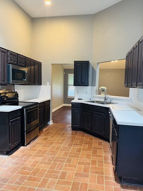 kitchen featuring appliances with stainless steel finishes, light countertops, a sink, and a towering ceiling