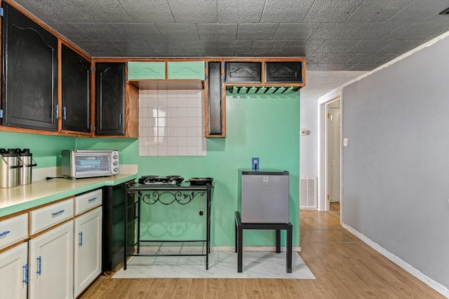 kitchen with a toaster, visible vents, baseboards, light wood-style flooring, and light countertops