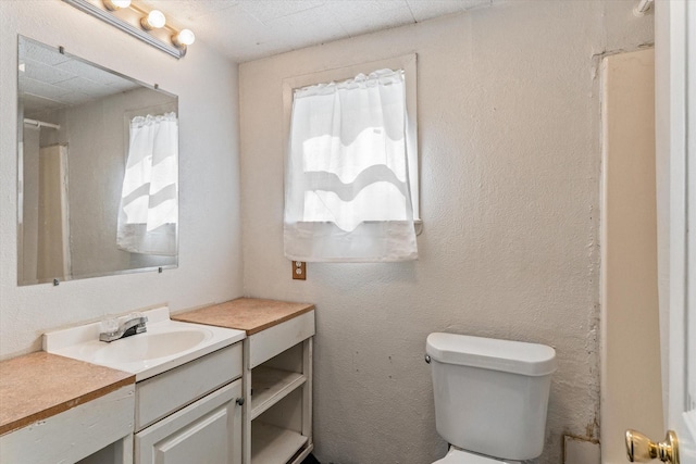 full bathroom featuring toilet, a textured wall, a shower with curtain, and vanity