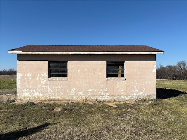 view of side of home featuring concrete block siding, a lawn, and roof with shingles