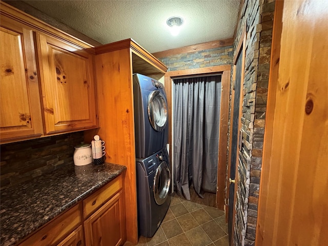 clothes washing area featuring a textured ceiling, laundry area, dark tile patterned floors, and stacked washing maching and dryer