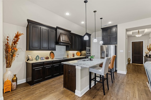 kitchen with a breakfast bar, light wood finished floors, stainless steel appliances, custom range hood, and backsplash