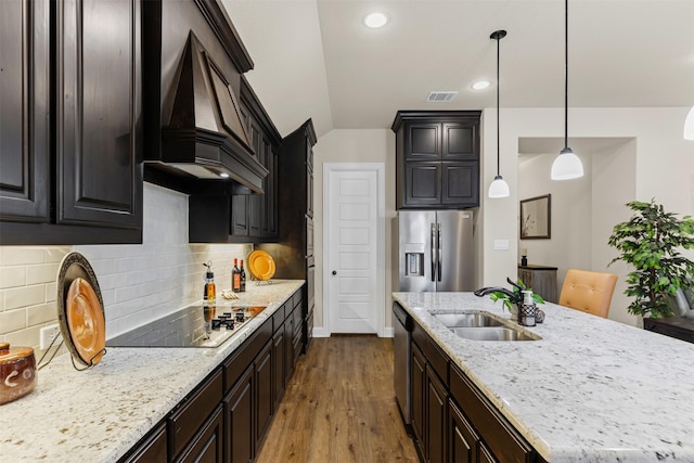 kitchen featuring stainless steel appliances, custom range hood, a kitchen island with sink, a sink, and wood finished floors