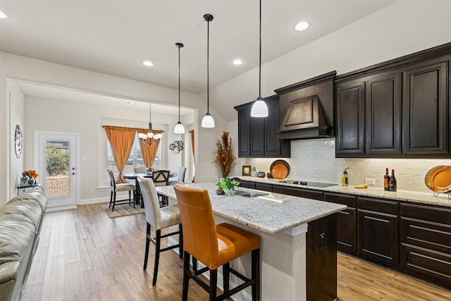 kitchen with light stone counters, a kitchen breakfast bar, light wood-style floors, custom exhaust hood, and tasteful backsplash