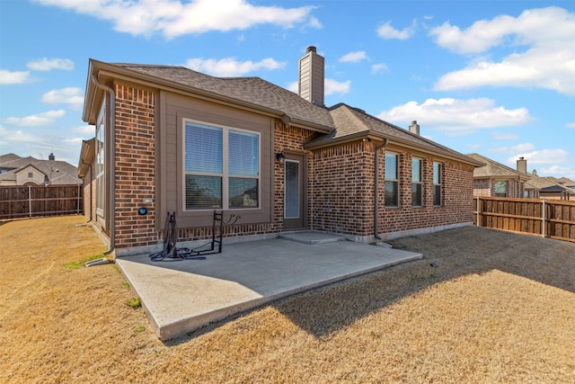 back of house featuring brick siding, a chimney, a patio area, and a fenced backyard