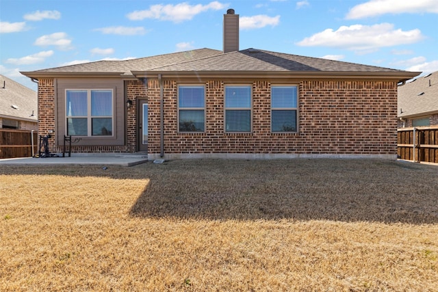 back of property with brick siding, a yard, a chimney, a patio, and fence