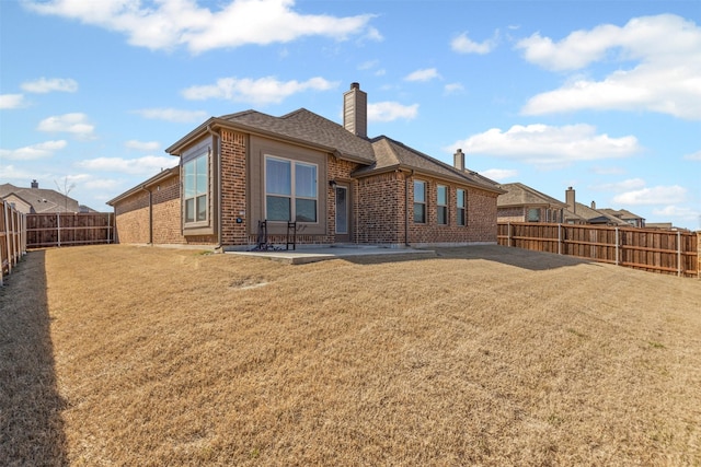 rear view of house featuring a patio, a fenced backyard, brick siding, a lawn, and a chimney