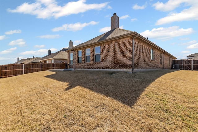 rear view of property featuring brick siding, a chimney, central air condition unit, a lawn, and a fenced backyard