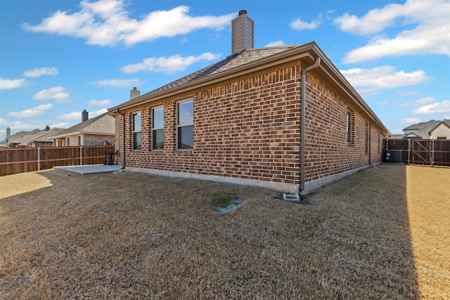 view of side of property featuring brick siding, a patio, a chimney, central air condition unit, and a fenced backyard