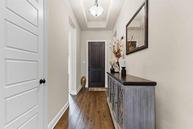 doorway to outside with a tray ceiling, dark wood-style flooring, and baseboards