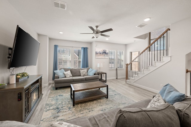 living area featuring light wood-style flooring, visible vents, stairway, and baseboards