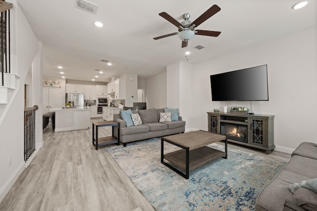 living room with light wood finished floors, a glass covered fireplace, visible vents, and recessed lighting