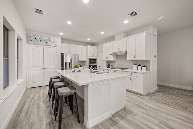 kitchen with visible vents, an island with sink, stainless steel appliances, under cabinet range hood, and a sink