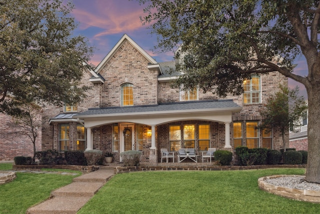 rear view of property featuring covered porch, brick siding, and a yard