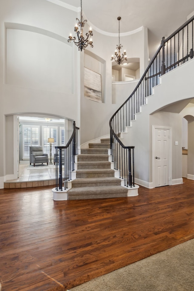 stairs with arched walkways, ornamental molding, wood finished floors, a chandelier, and baseboards