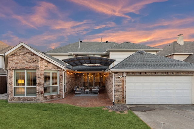 back of property with roof with shingles, a yard, brick siding, an attached garage, and driveway