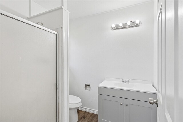 bathroom with toilet, a stall shower, wood finished floors, baseboards, and vanity