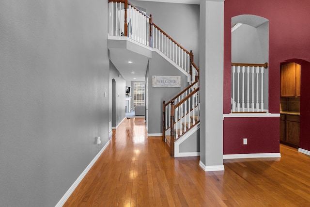 stairway featuring arched walkways, wood-type flooring, a towering ceiling, and baseboards