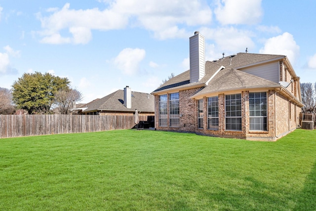 back of house with brick siding, a lawn, a chimney, and a fenced backyard